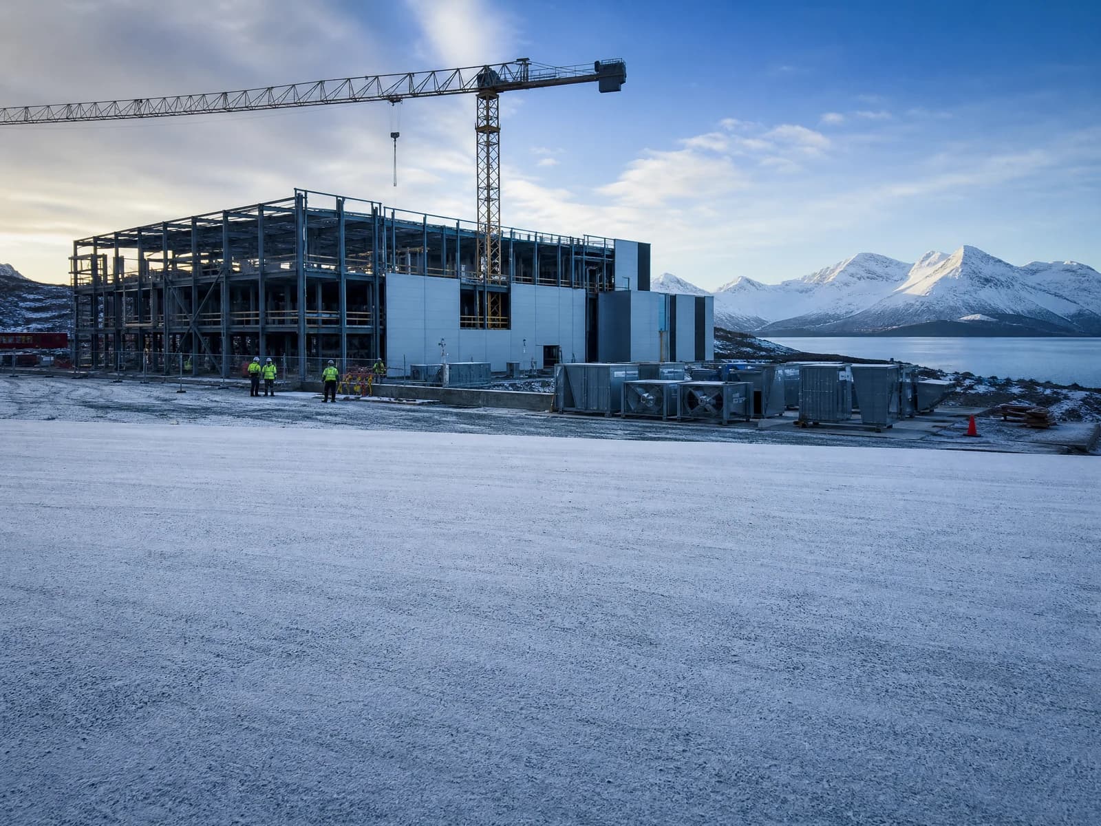 A data center under construction in a snowy Norwegian landscape, steel frame partly clad and a crane on site